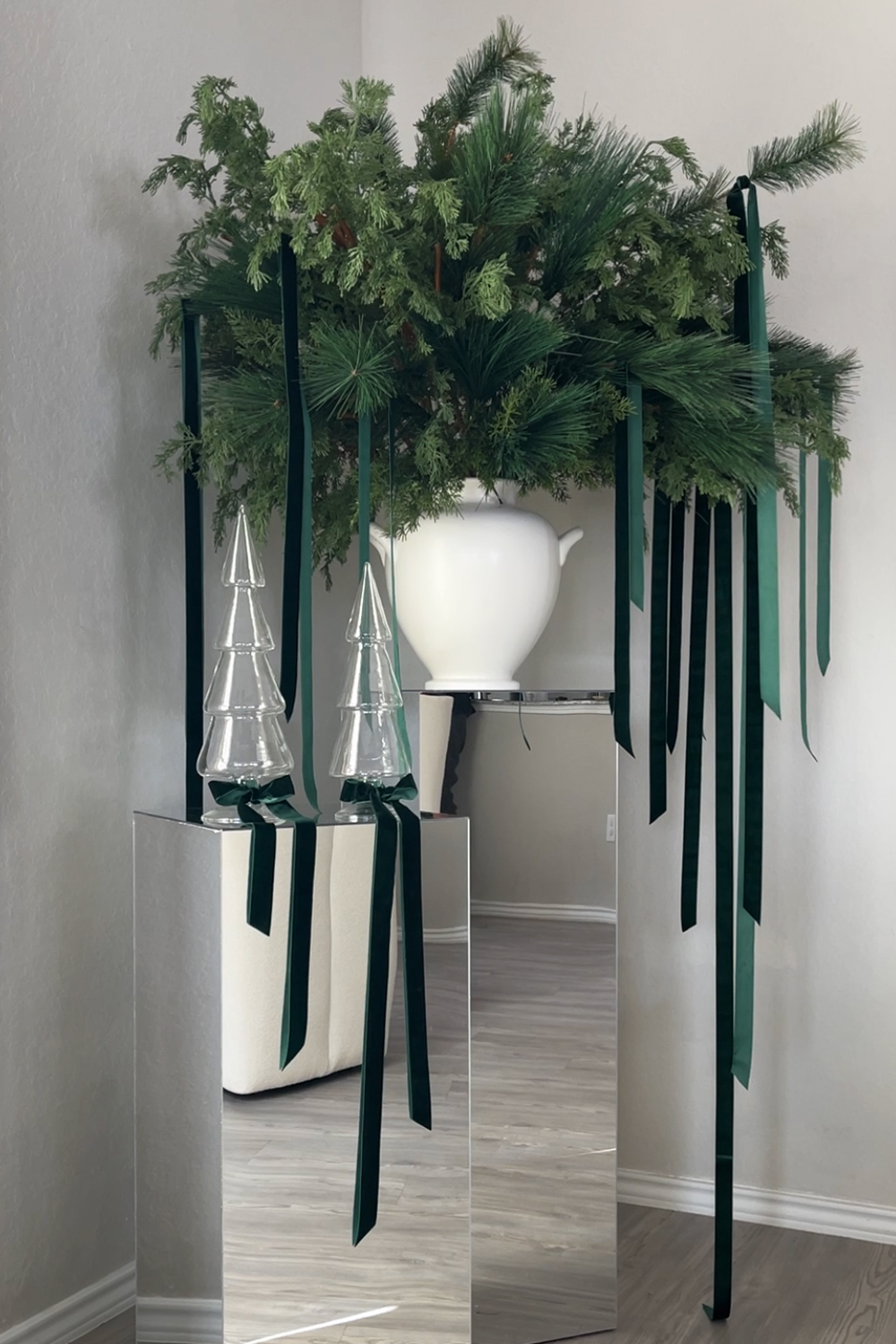 Learn how to design a modern Christmas floral arrangement with cedar and pine faux greenery and branches, velvet ribbon, and mirrored pedestals. Add a touch of elegance and sparkle to your holiday decor!