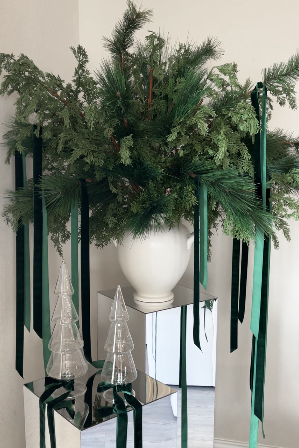 Learn how to design a modern Christmas floral arrangement with cedar and pine faux greenery and branches, velvet ribbon, and mirrored pedestals. Add a touch of elegance and sparkle to your holiday decor!